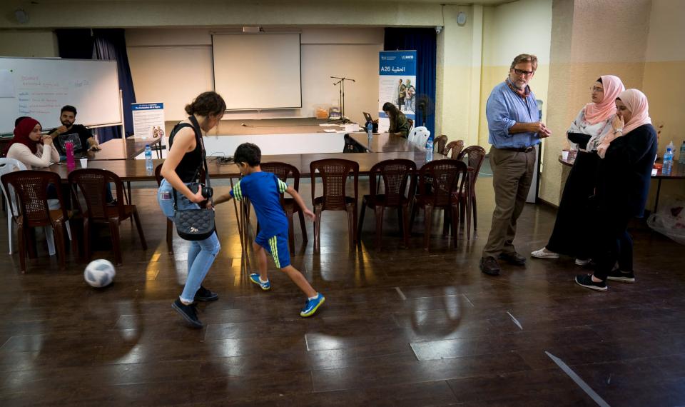 Several people in a room talking in small groups, two people playing soccer