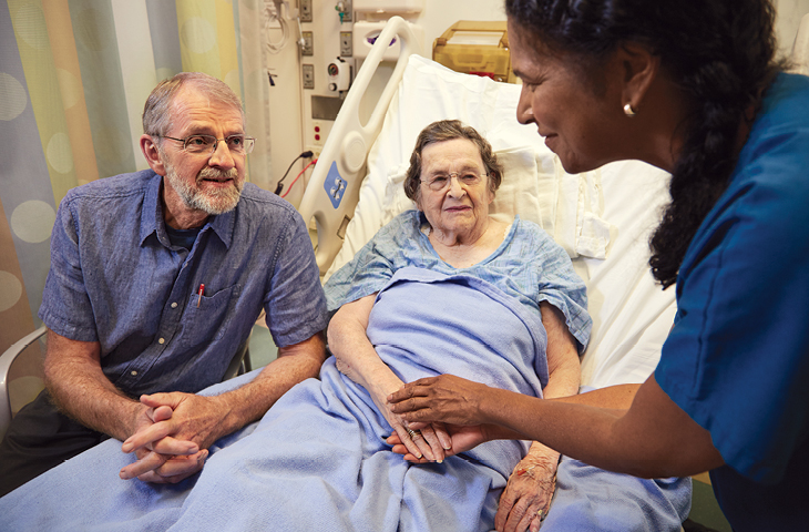 A caregiver at UC Davis holding hands with patient and speaking with a patient's loved one