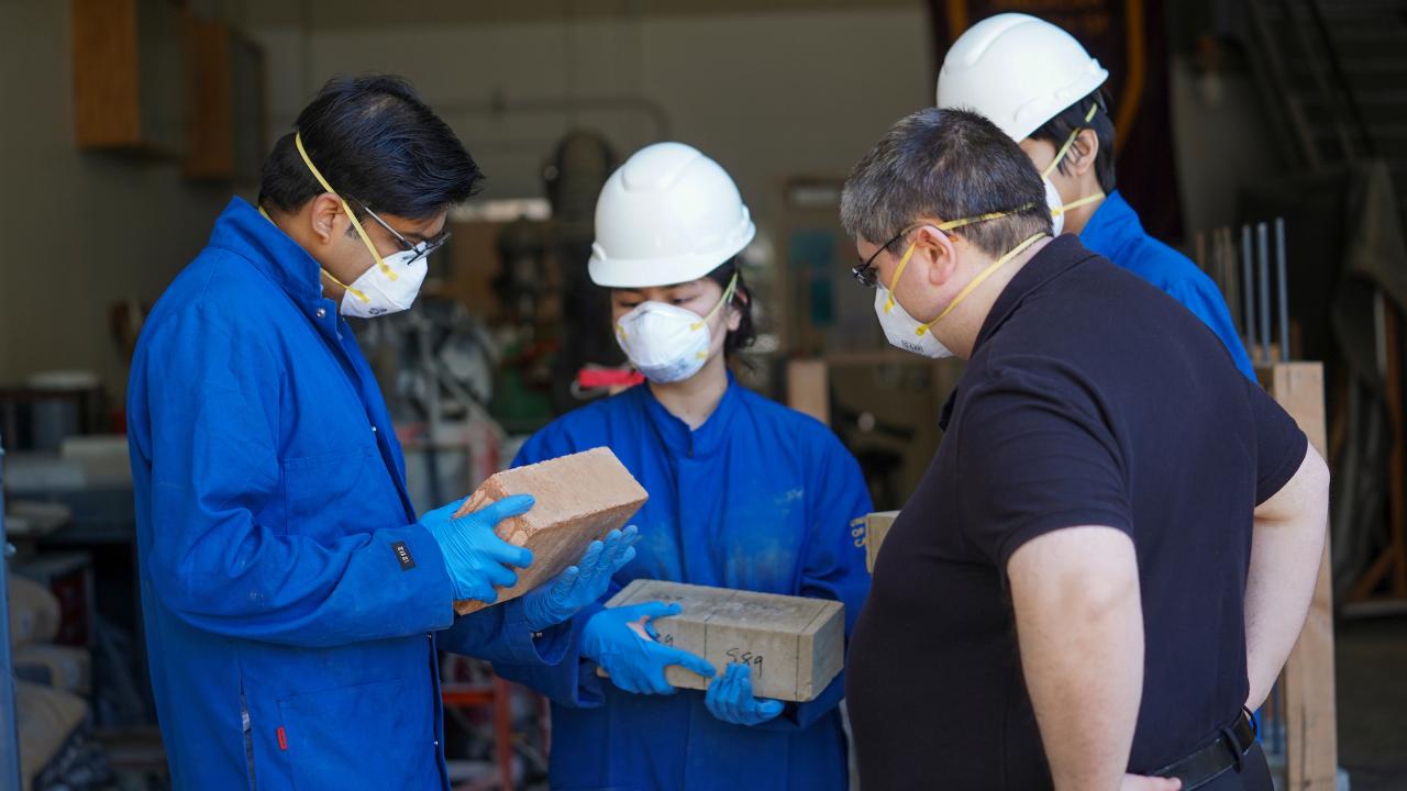 Four people looking at blocks, all wearing face masks, two wearing hard hats.