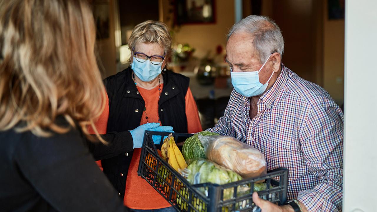 Health experts recommend assigning roles to caregivers who support from inside or outside the home. Two people receiving basket of food from another person