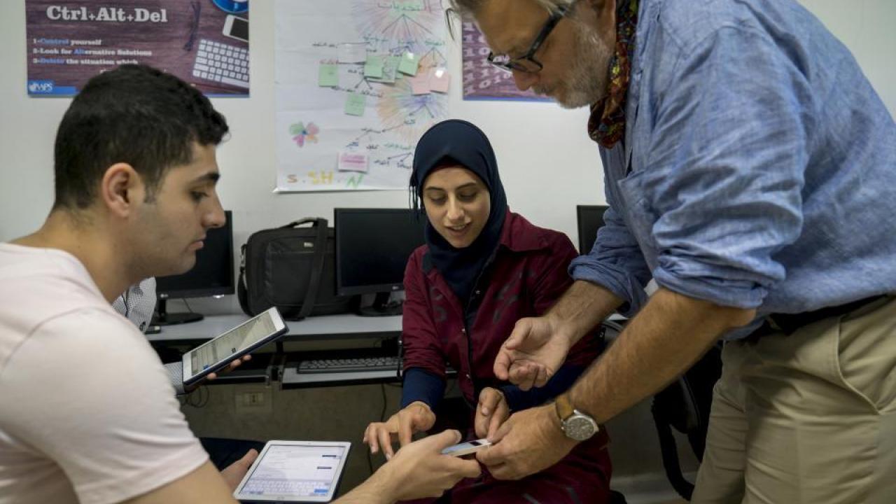 Keith David Watenpaugh, right, a professor and director of UC Davis Human Rights Studies, and Eslam Abo Alhawa, center, help Ali Almarzouki register for the Article 26 Backpack in Lebanon's Bekaa Valley. (Joe Proudman/UC Davis) Three people looking at a cell phone