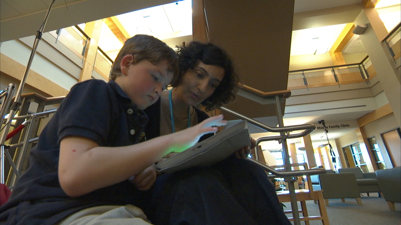 A child and an adult sitting down while looking at a tablet