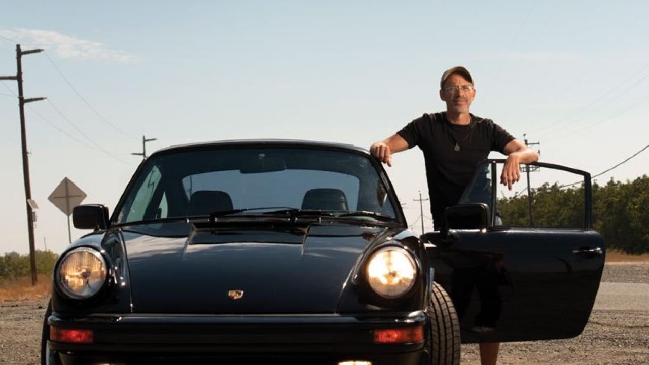 Man standing outside a black Porsche on the side of a road.