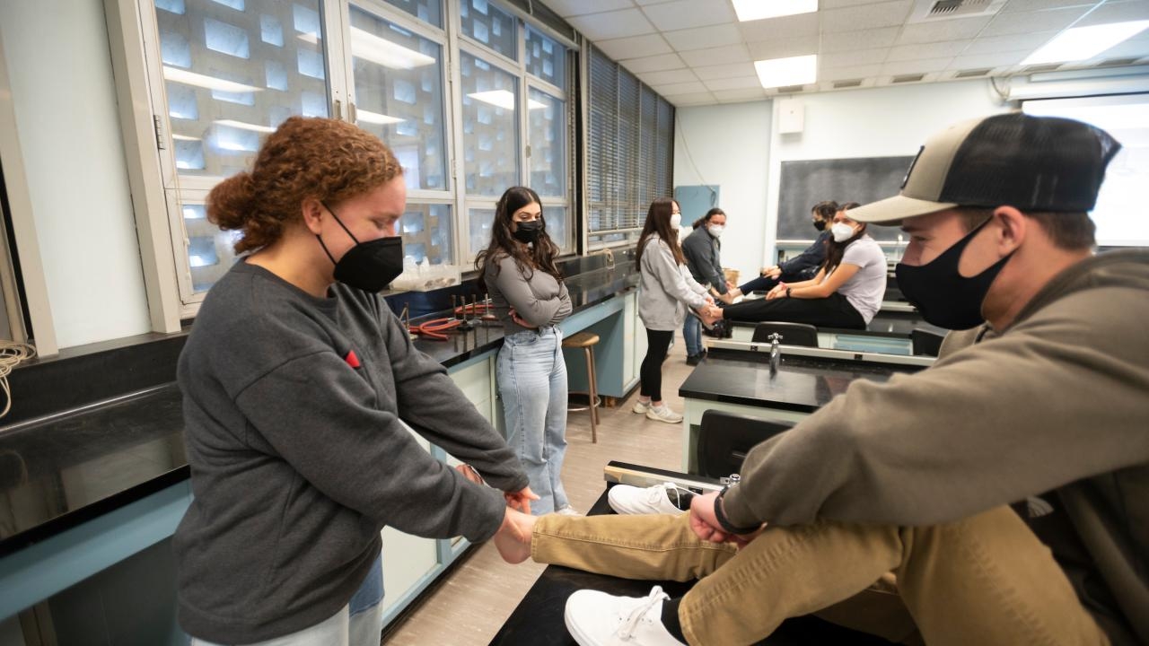 Student conducting an ankle examination by touching another students ankle to inspect.