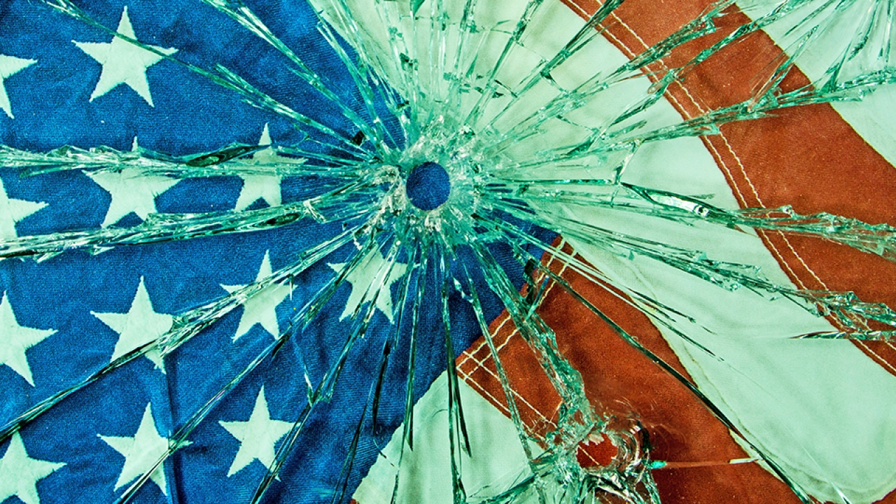 American flag behind a sheet of glass shattered from a bullet hole