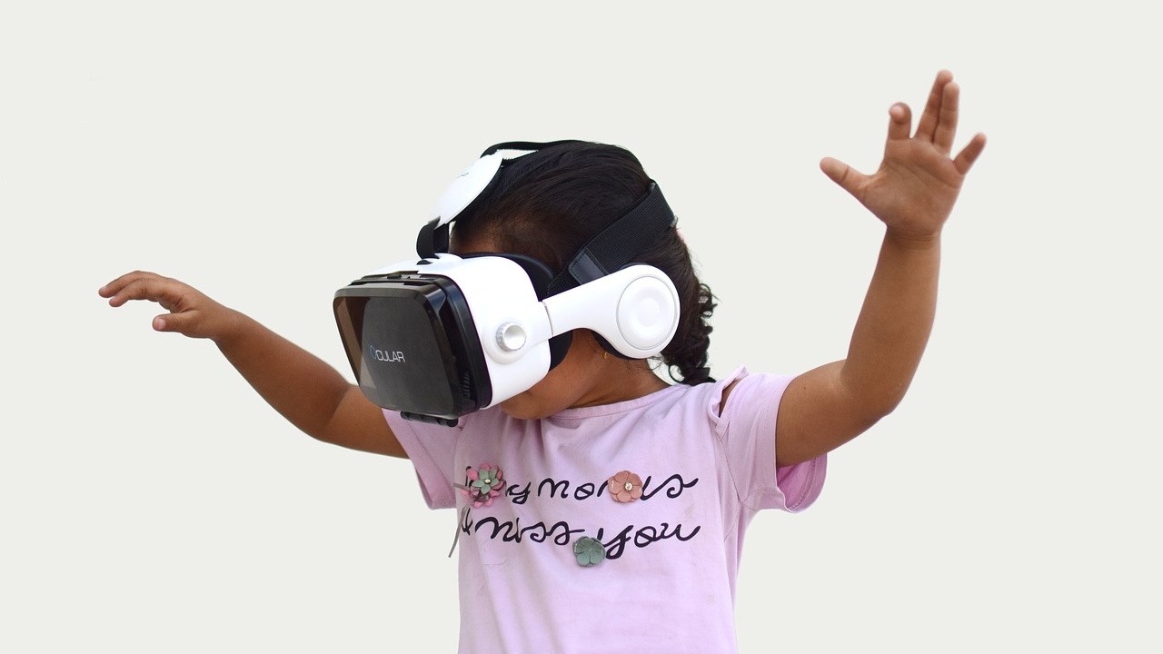 A child wearing virtual reality goggles with their hands in the air.