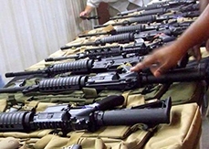 About 10 black firearms of the same type on a table.
