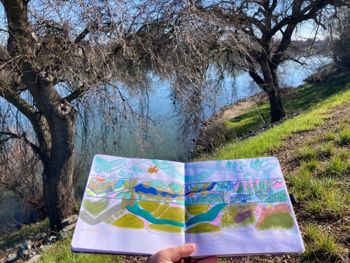 Photo of sketchbook with mural designs. Background is Sacramento river.