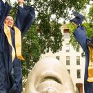 Students in commencement robes jumping in front of an egghead