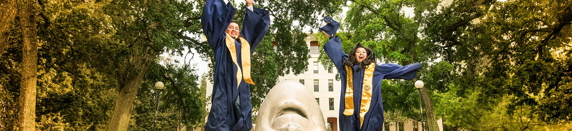 Two UC Davis graduating students jumping in front of an egghead